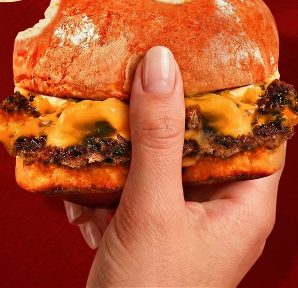 A Le SMASH burger held in one hand, the patties visible in profile