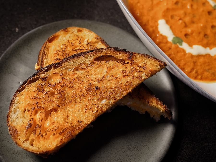 Grilled cheese cut in half beside a bowl of tomato soup