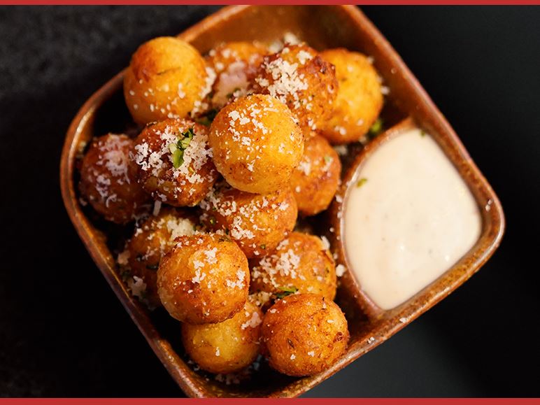 Fried potato balls in a wooden dish with a dip
