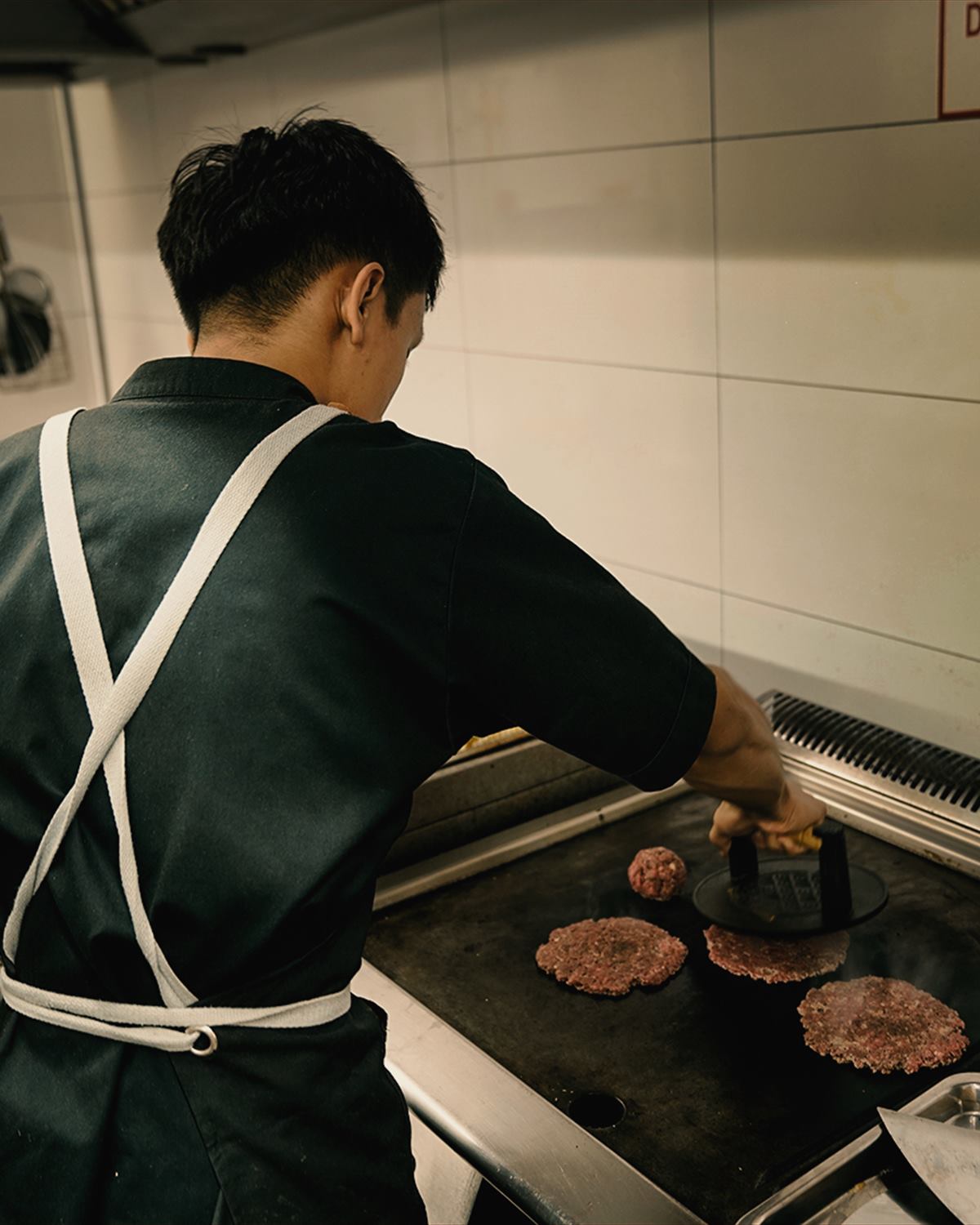 A cook pressing balls of beef flat on the plancha