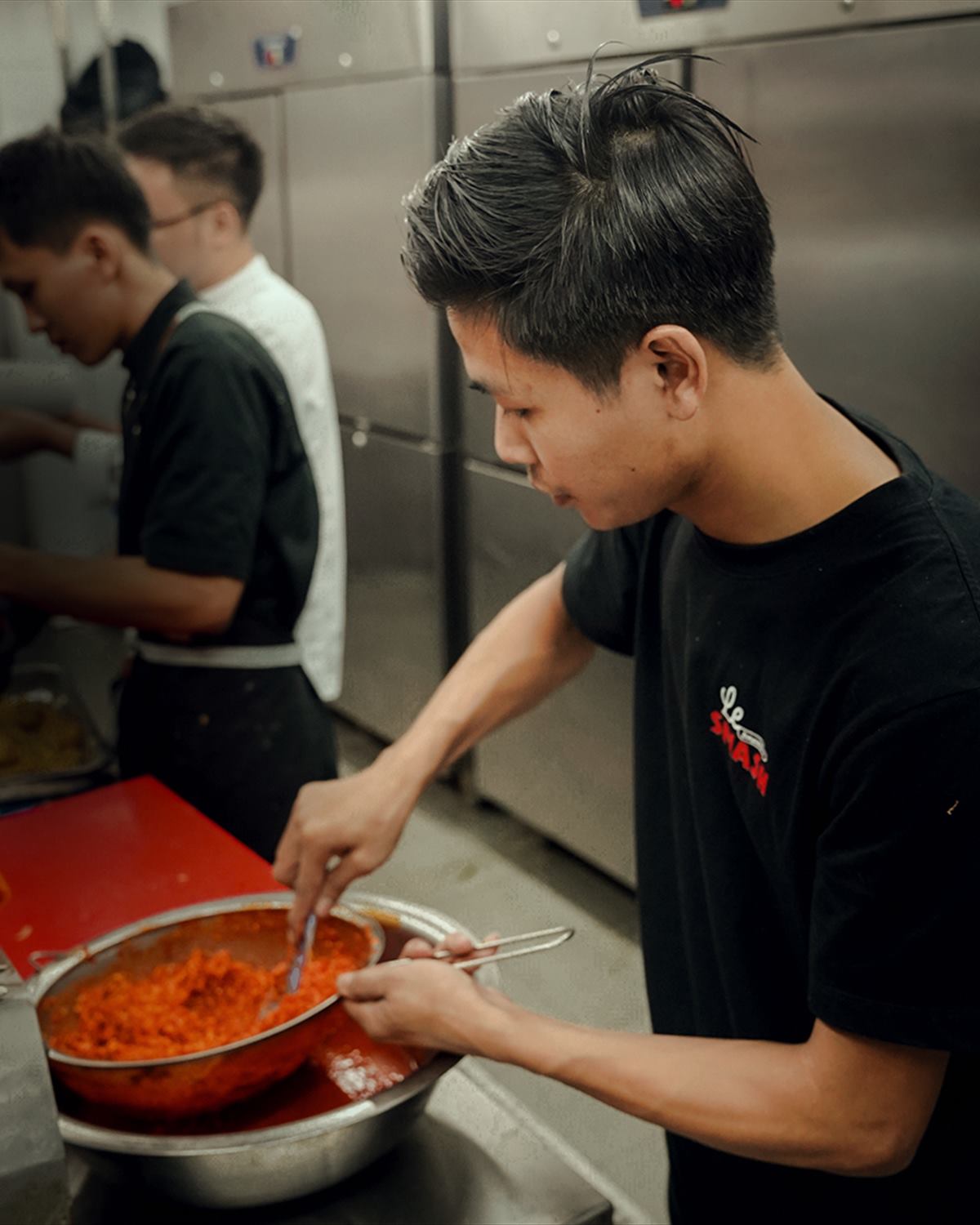 A cook stirring a tray of sauce in the kitchen