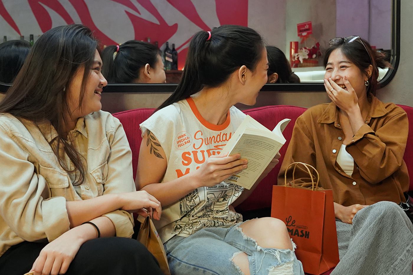 Friends on the red banquette with shopping bags and a menu