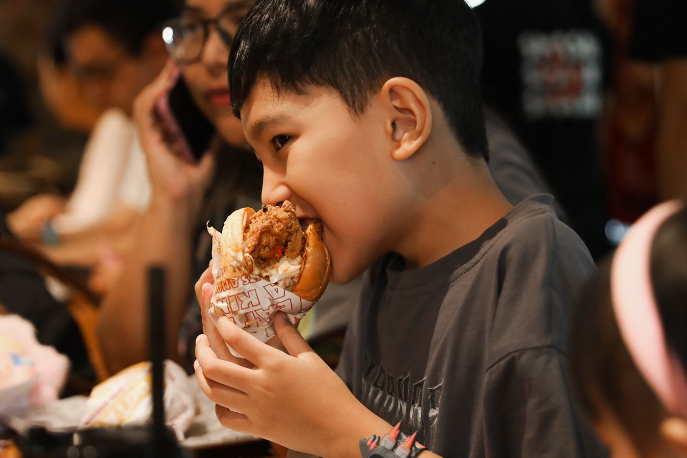 A boy taking the first bite of a burger at the counter