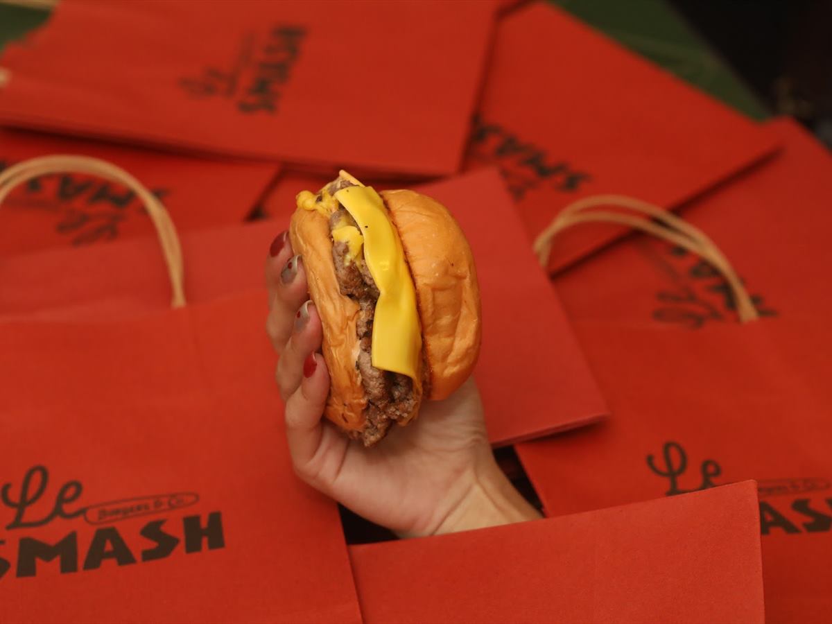 A burger held over a table of red Le SMASH bags
