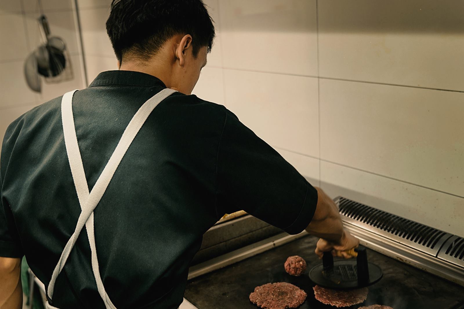 A cook pressing balls of beef flat on the plancha